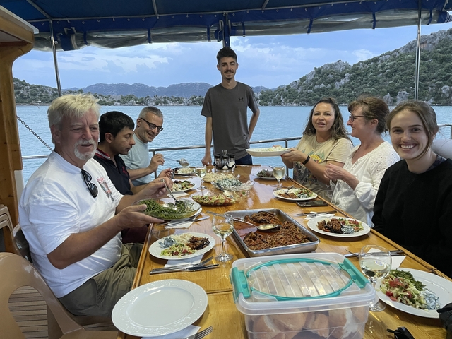       People enjoying a meal on a boat with a scenic background.
  