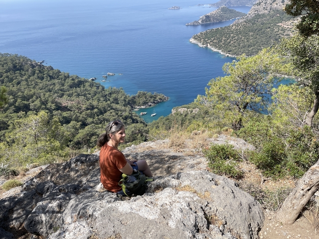 Person sitting on a cliff overlooking a bay.