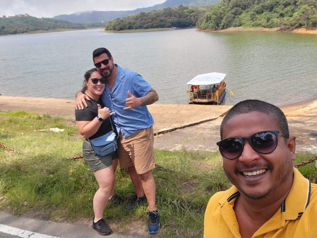 Selfie of people by a lake with a small boat in the background.