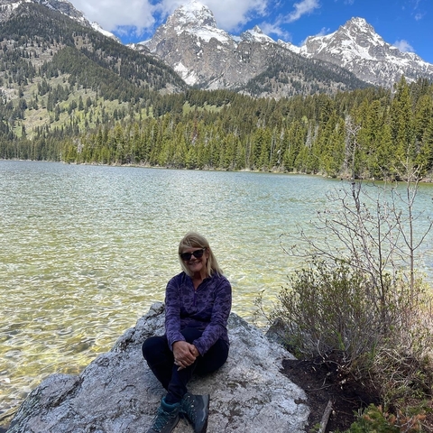 Woman sitting by a lake with trees in the background.
