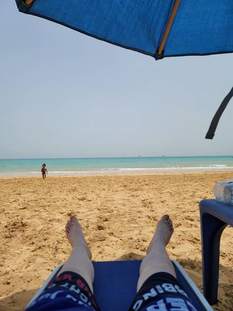 Feet resting on a beach with sea and sky in the background.