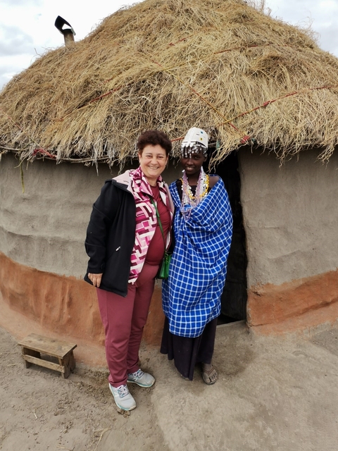 Two women posing in front of a traditional hut.