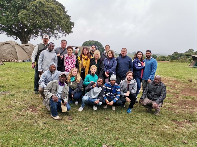 A group of people standing on a grassy field with tents in the background.