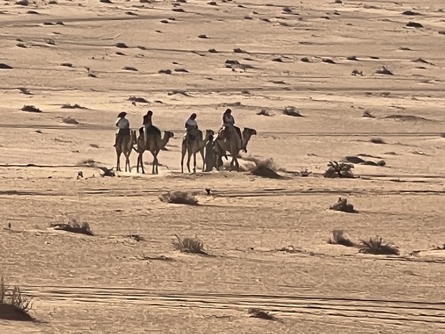 Camel riders in a vast desert landscape.