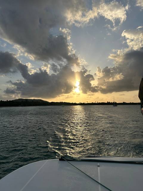 Sun setting over water with boats and clouds.