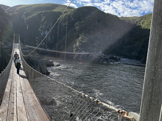 People crossing a rope bridge over a river in the mountains.