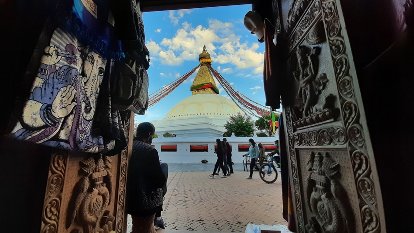       People walking towards a stupa viewed through a doorway.
  