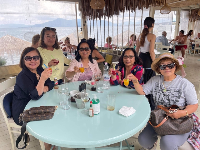       Group of people enjoying drinks and food at a seaside café.
  