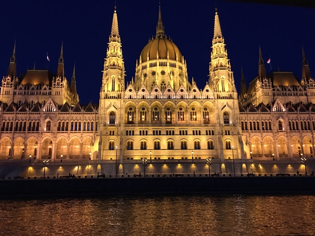       Night view of an illuminated Gothic building along a river.
  