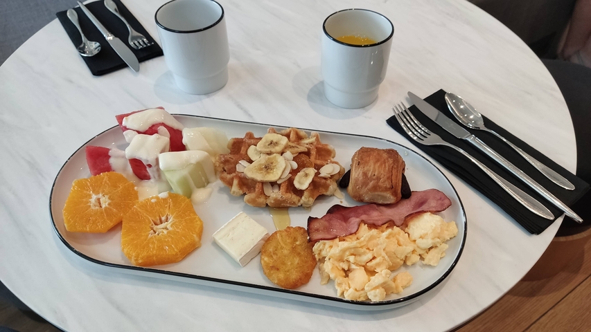       A breakfast plate with a variety of foods including waffles, fruits, and scrambled eggs on a table.
  