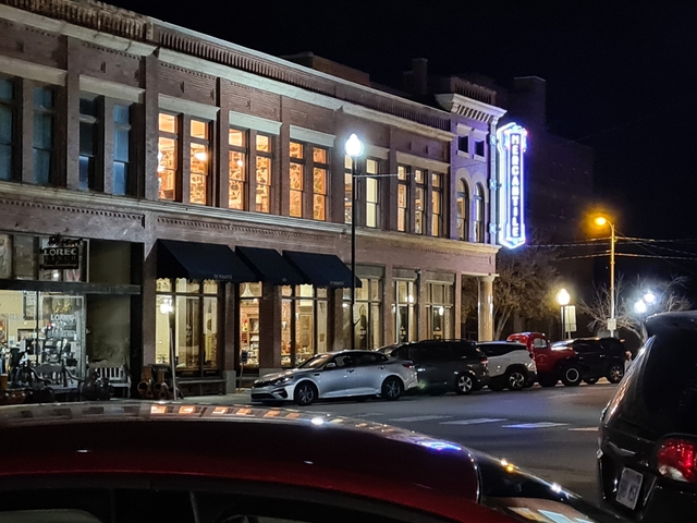 Nighttime urban street view with cars and glowing sign.