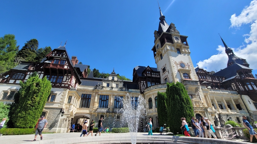 A grand, historic castle with people and fountains in front.