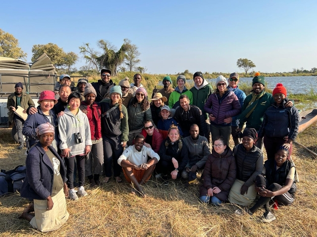       Large group posing on the shore with a river in the background.
  