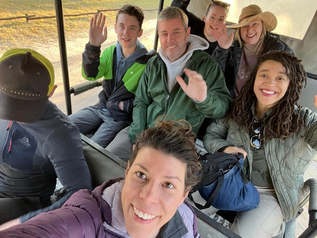       People sitting in a safari vehicle waving.
  