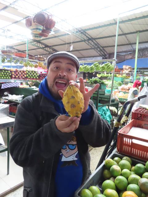       A man holding a fruit at a market stall.
  