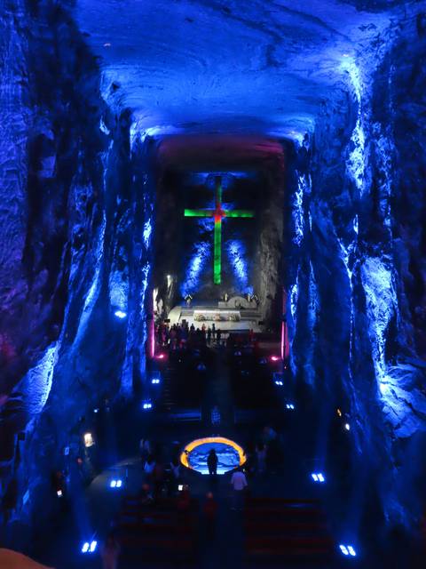       A cave with illuminated colorful lights and a cross in the background.
  