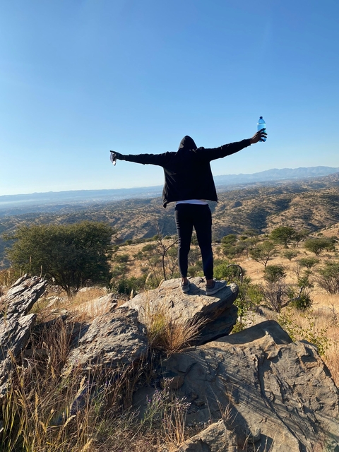 Person with arms outstretched standing on a rocky hill.