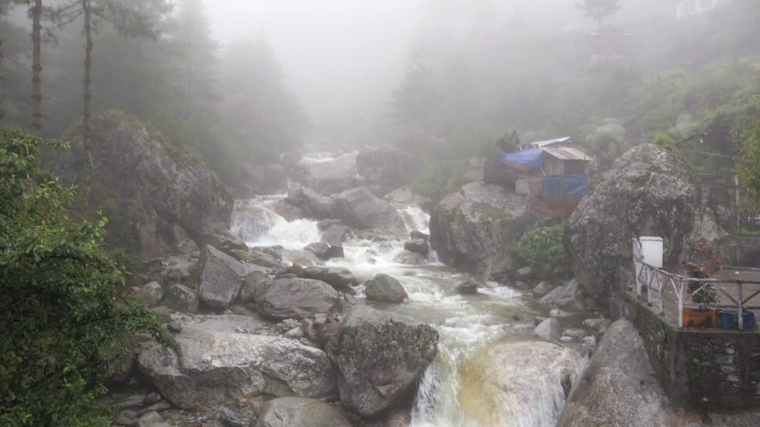 A misty mountain stream with flowing water and large boulders.