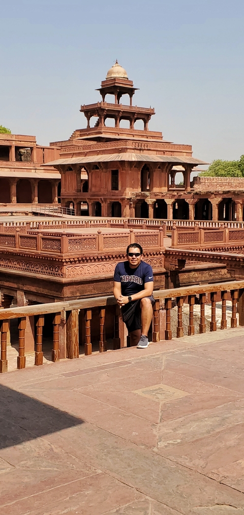 A man sitting on the stone railing of a historical fort with intricate carvings.