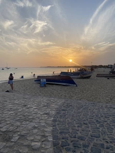 Sunset on a sandy beach with boats and people in the distance.