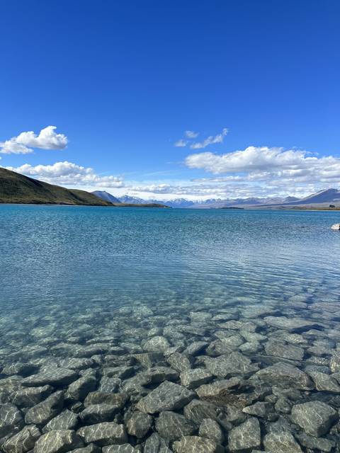       Rocky lakeshore with mountains and clear sky.
  