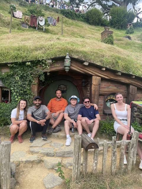       Group of people posing in front of a Hobbit house.
  