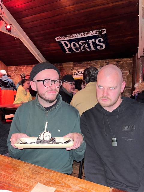       Two men indoors holding a plate, looking engaged.
  