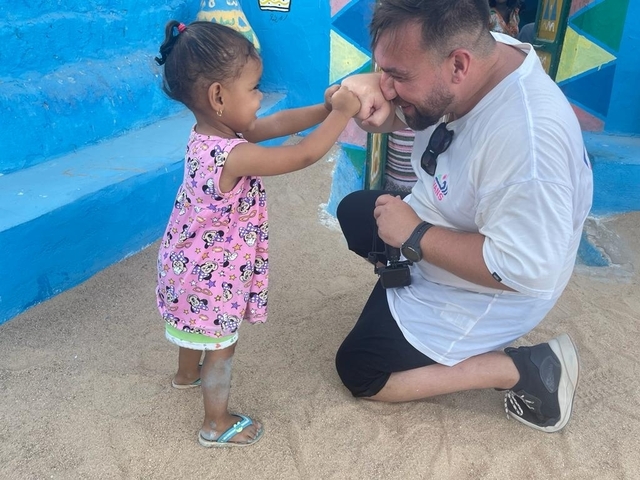 Person kneeling and interacting with a young child in a colorful outdoor setting.