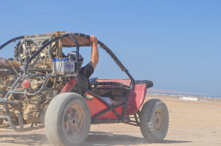 Person driving a dune buggy in a desert landscape.