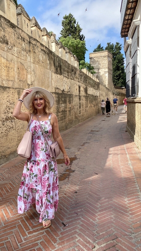       Person holding a hat on a cobblestone street with historic architecture.
  