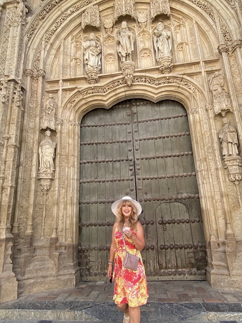       A woman in a white hat in front of an ornate wooden door with sculptures.
  