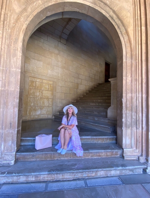 Person sitting on steps in a historical building wearing a hat.
