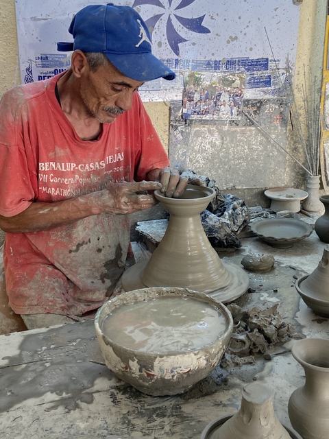 Potter shaping clay on a wheel in a workshop.
