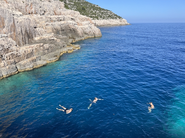       People swimming near rocky cliffs with clear blue water.
  