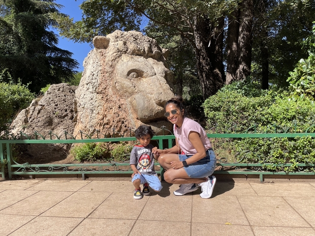 Woman and child posing in front of a lion-shaped rock sculpture.