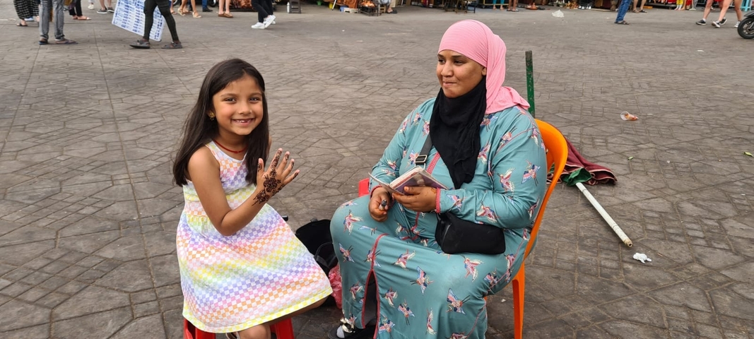 Child showing henna tattoo while sitting beside an artisan.