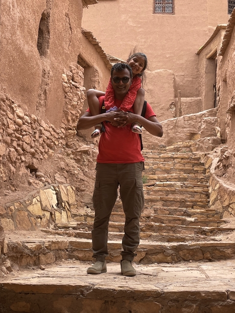 Man carrying a child on his shoulders in a stone alley.