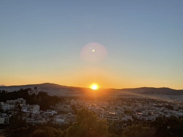       Sunset over a cityscape with hills in the background.
  