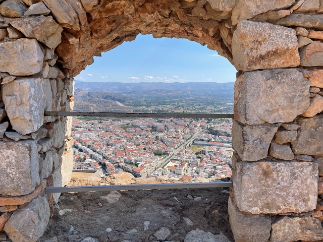       View through a stone window showing a town with distant mountains.
  