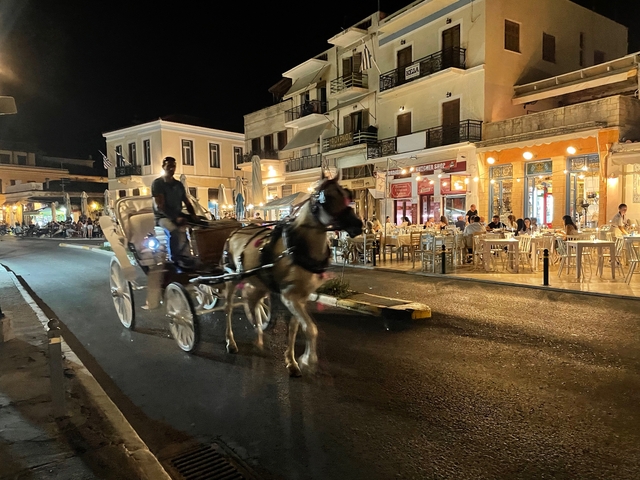       Horse-drawn carriage moving through a lively street at night.
  