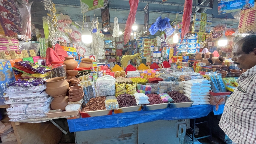       Colorful market stall with jars, spices, and various goods, viewed from inside a market.
  