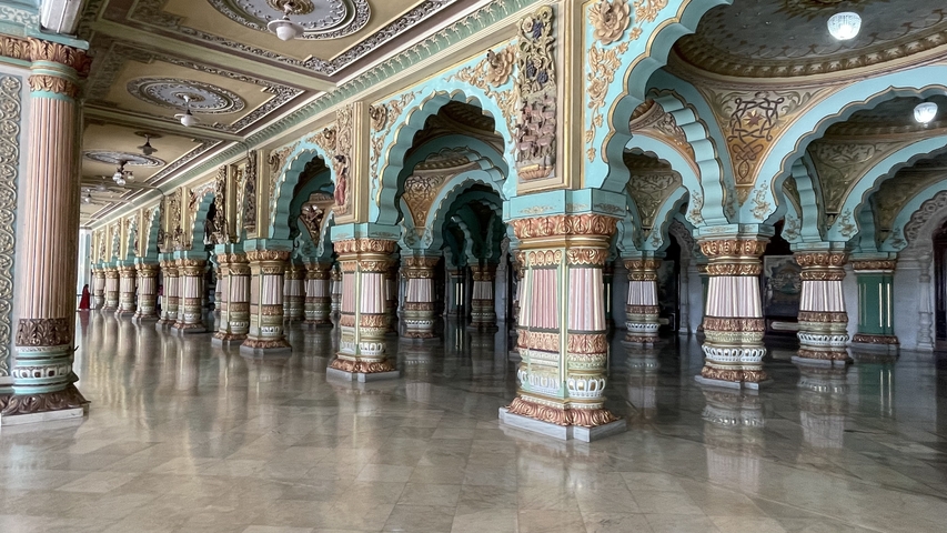       Ornate hall with rows of intricately decorated arches and columns reflecting on a shiny floor.
  