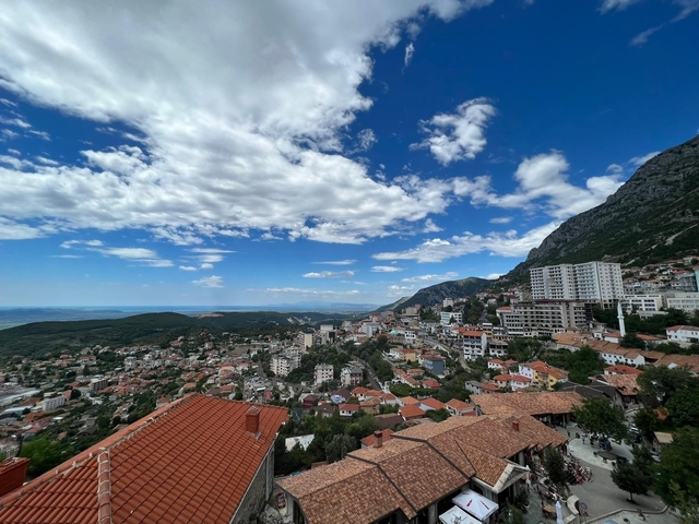       Panoramic view of a city with mountains and a partly cloudy sky.
  