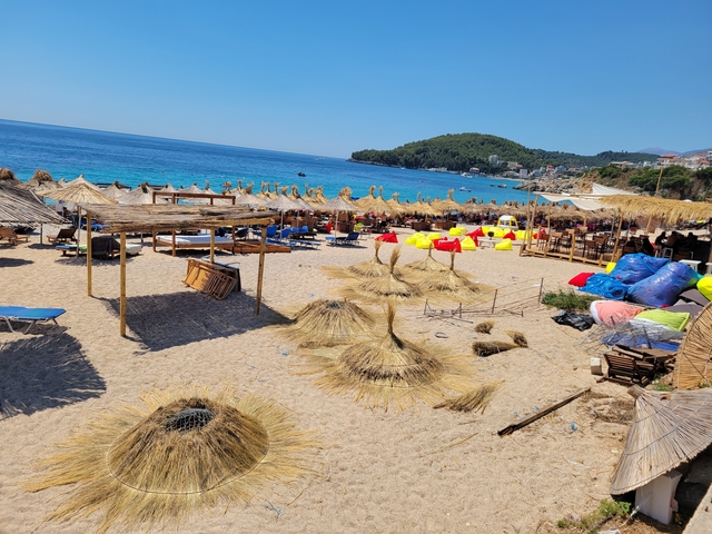       Beach with straw umbrellas and clear blue sea under a bright sky.
  