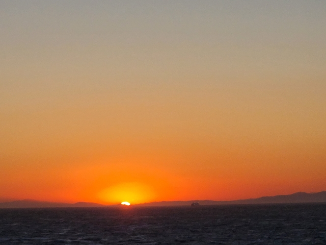      Sunset over the ocean with a ship on the horizon.
  