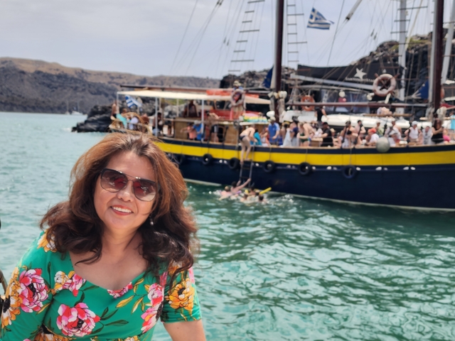       Woman posing on a boat with people swimming nearby.
  