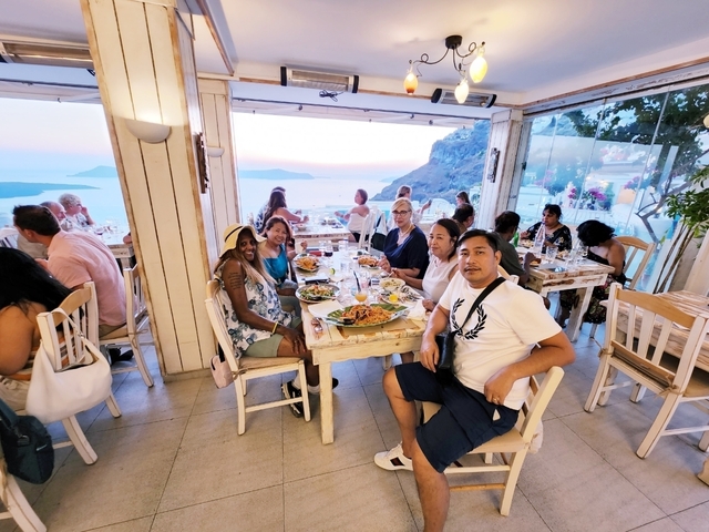       Group dining at a seaside restaurant with a scenic view.
  