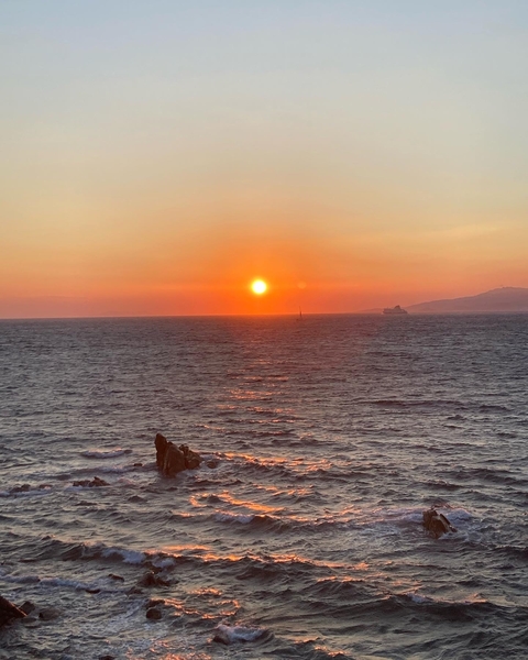 Sun setting over the ocean with a distant ship.
