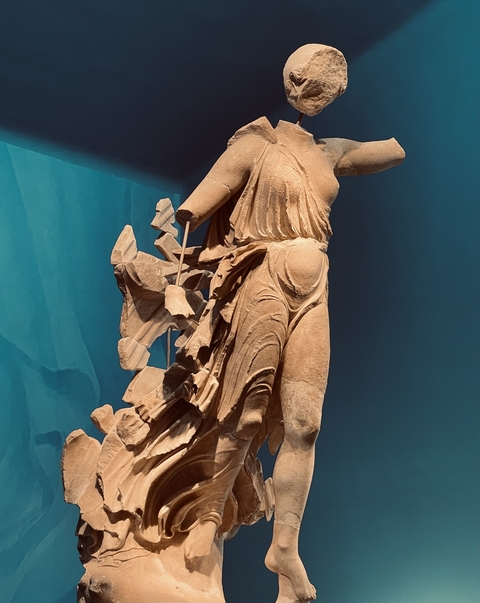 Statue of a figure with a broken arm in a museum setting.