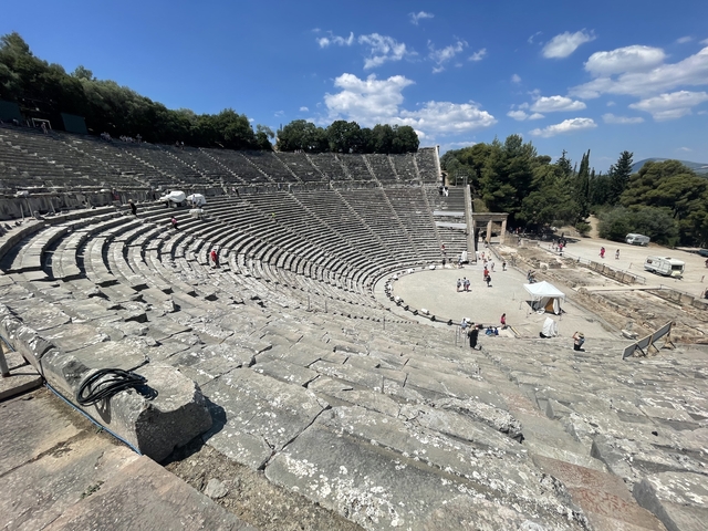       Ancient Greek amphitheater with scattered tourists exploring.
  